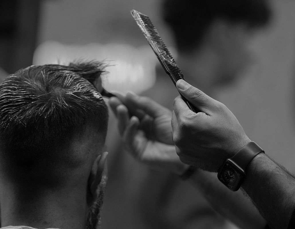 Barber combing through a taper fade, seen from behind the chair