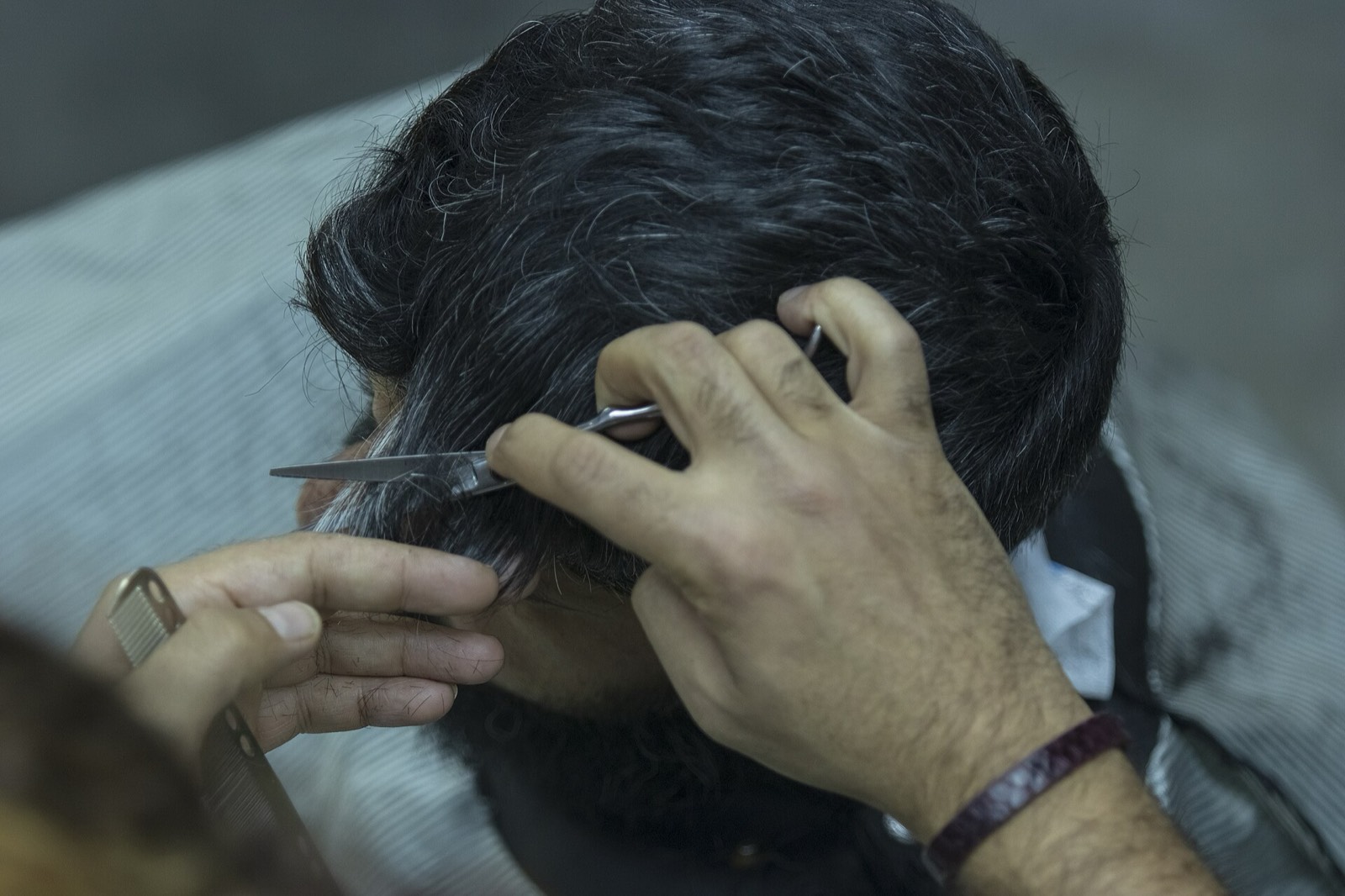 Close-up of a barber's hands trimming around a client's ear with scissors