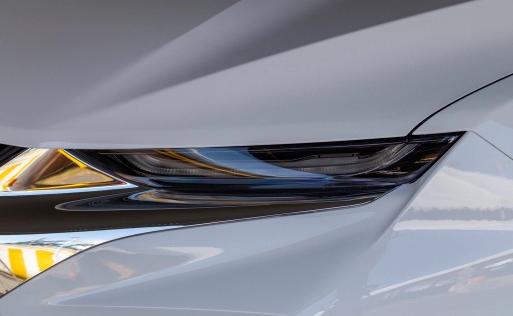 Close-up of a pale gray hood edge and a slim headlight under soft light