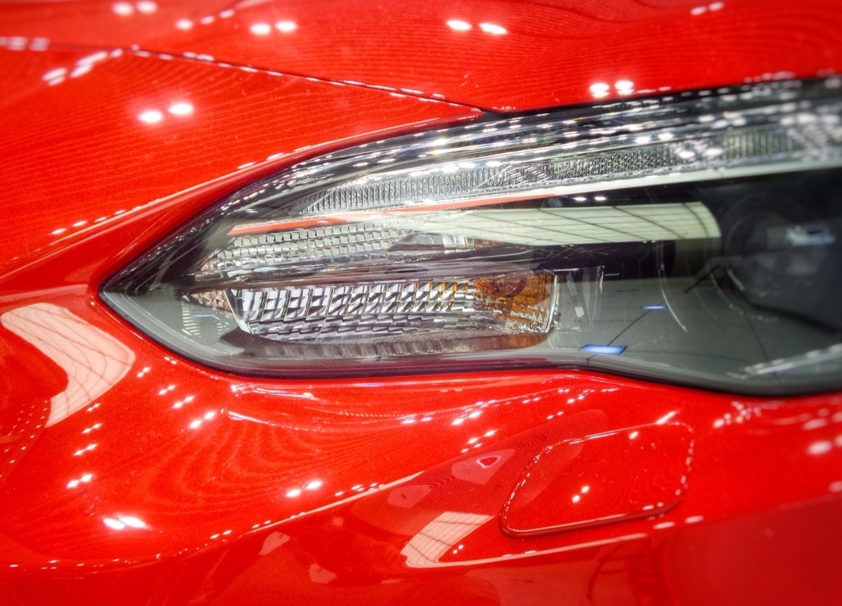 Close-up of a glossy red fender and headlight reflecting rows of shop lights