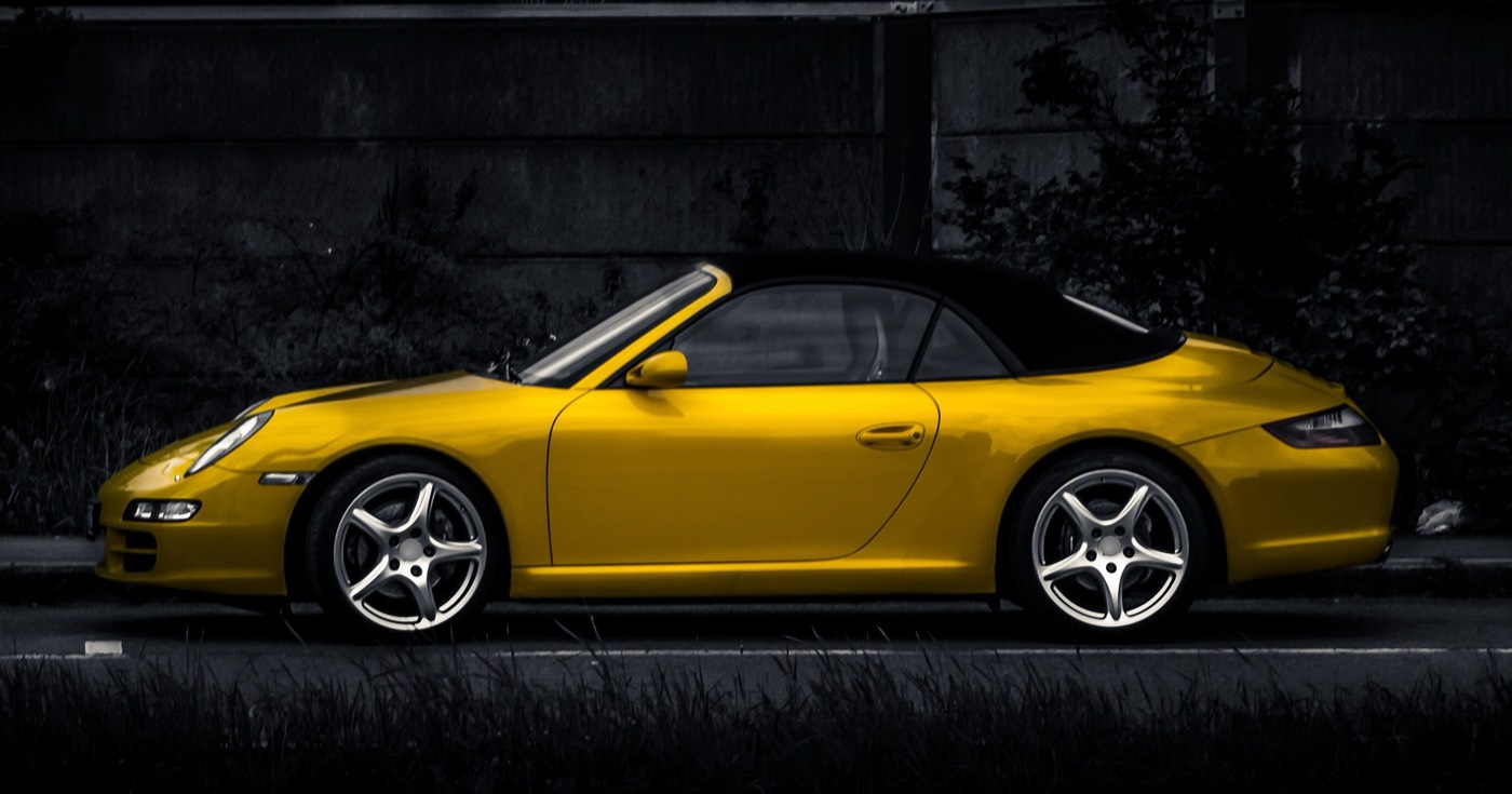 Side view of a bright yellow convertible sports car on a dark street