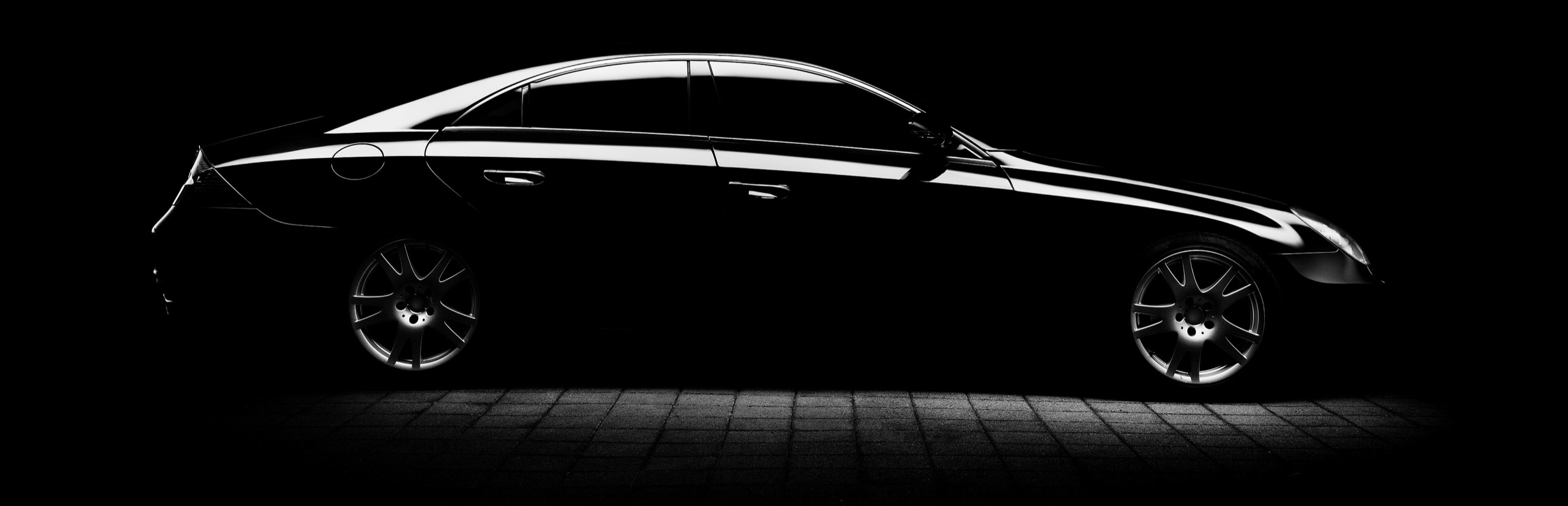 A dark, glossy sports car under studio lights, its paint reflecting long bars of light